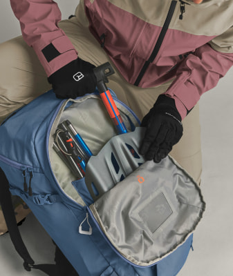 Eine Person in einer Skijacke packt Ausrüstung in einen Rucksack. Eine Person in einer Skijacke packt Ausrüstung in einen Rucksack.