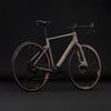 Ein braunes Cube Gravelbike mit schwarzen Felgen und Lenkern vor dunklem Hintergrund.
