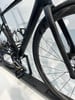 Ein schwarzer Rennradrahmen mit Carbonfelgen und Pedalen.