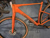 Ein orangefarbenes Cannondale Gravelbike mit beigen Reifen und schwarzem Lenker.
