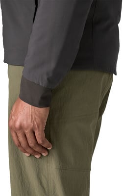 Detail einer Hand und eines Ärmels einer dunklen Jacke über grünen Hosen.