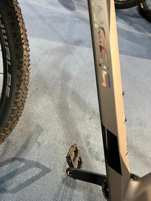 Detail eines Fahrradrahmens mit Logo und Pedal auf blauem Teppich. Detail eines Fahrradrahmens mit Logo und Pedal auf blauem Teppich.