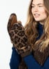 Eine junge Frau mit langen blonden Haaren trägt leopardfarbene Fäustlinge und einen blauen Pullover.