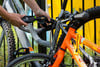 Hände schließen ein Fahrrad mit einem Kettenschloss mit Zahlencode ab.