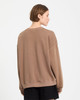 Ein Mädchen in einem braunen Sweatshirt und schwarzen Shorts steht mit dem Rücken zur Kamera.
