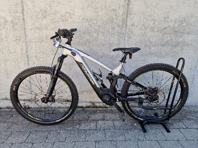 Silber-schwarzes E-Mountainbike mit Federung auf einem Ständer. Silber-schwarzes E-Mountainbike mit Federung auf einem Ständer.