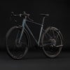 Grauer Gravelbike-Rahmen mit Schutzblechen und Gepäckträger vor schwarzem Hintergrund.