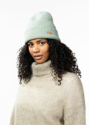Junge Frau mit lockigem Haar trägt eine hellgrüne Mütze und einen beige Pullover. Junge Frau mit lockigem Haar trägt eine hellgrüne Mütze und einen beige Pullover.