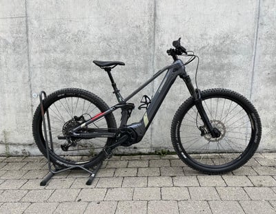 Graues E-Mountainbike auf einem Ständer vor einer Wand.