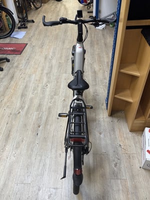 Silbernes E-Bike mit schwarzem Sattel und Gepäckträger auf Holzboden. Silbernes E-Bike mit schwarzem Sattel und Gepäckträger auf Holzboden.