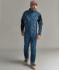 Ein Mann in blauer Skibekleidung und rosafarbener Mütze steht vor grauem Hintergrund.