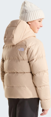 Mädchen in einer beigen Daunenjacke und Strickmütze mit The North Face Logo.