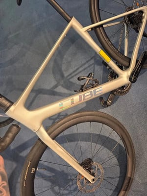 Silberner Fahrradrahmen mit CUBE-Logo und schwarzen Rädern.
