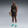 Ein Mann in schwarzem Tanktop und Shorts hält eine Wasserflasche und trägt Laufschuhe.
