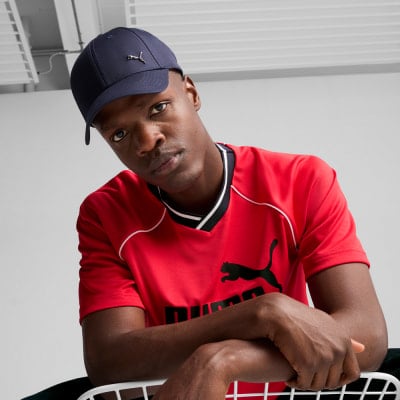 Ein Mann in einem roten T-Shirt und einer dunkelblauen Kappe mit Puma-Logo.