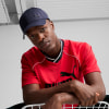 Ein Mann in einem roten T-Shirt und einer dunkelblauen Kappe mit Puma-Logo.