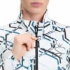 Eine Frau schließt eine Jacke mit geometrischem Muster und Kronenlogo.