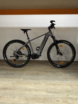 Graues Genesis E-Bike mit schwarzen Rädern auf Holzboden.
