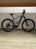 Graues Genesis E-Bike mit schwarzen Rädern auf Holzboden.