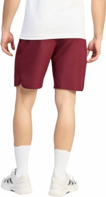 Ein Mann in einem weißen T-Shirt und burgunderfarbenen Shorts steht vor weißem Hintergrund.