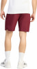 Ein Mann in einem weißen T-Shirt und burgunderfarbenen Shorts steht vor weißem Hintergrund.