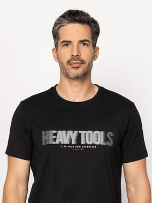 Fekete pólót viselő férfi HEAVY TOOLS felirattal és szlogennel. Fekete pólót viselő férfi HEAVY TOOLS felirattal és szlogennel.