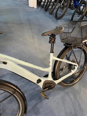 Ein hellgraues Specialized E-Bike mit Korb und Schutzblechen auf Teppich. Ein hellgraues Specialized E-Bike mit Korb und Schutzblechen auf Teppich.