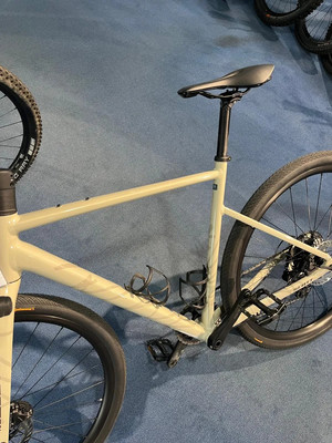 Ein beiges Gravelbike mit schwarzem Sattel und schwarzen Rädern auf einem blauen Teppich. Ein beiges Gravelbike mit schwarzem Sattel und schwarzen Rädern auf einem blauen Teppich.