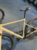 Ein beiges Gravelbike mit schwarzem Sattel und schwarzen Rädern auf einem blauen Teppich.