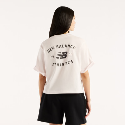 Frau in einem rosa T-Shirt mit New Balance Logo und schwarzen Shorts.