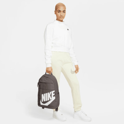 Ein Model hält einen dunkelgrauen Rucksack mit Nike-Logo auf weißem Hintergrund. Ein Model hält einen dunkelgrauen Rucksack mit Nike-Logo auf weißem Hintergrund.