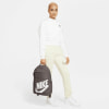 Ein Model hält einen dunkelgrauen Rucksack mit Nike-Logo auf weißem Hintergrund.
