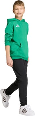 Junge in grüner Kapuzen-Sweatshirt und schwarzer Hose, weiße Sneaker.