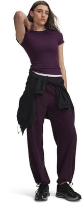 Model in dunkelviolettem Oberteil und Jogginghose mit schwarzer Jacke um die Taille.