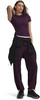 Model in dunkelviolettem Oberteil und Jogginghose mit schwarzer Jacke um die Taille.