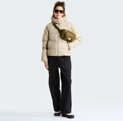 Eine Frau in einer beigen Daunenjacke und schwarzen Hose mit einer Bauchtasche. Eine Frau in einer beigen Daunenjacke und schwarzen Hose mit einer Bauchtasche.