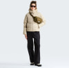 Eine Frau in einer beigen Daunenjacke und schwarzen Hose mit einer Bauchtasche.
