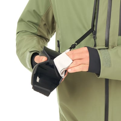 Eine Person reinigt eine Brille mit einem grauen Tuch an einer grünen Jacke. Eine Person reinigt eine Brille mit einem grauen Tuch an einer grünen Jacke.