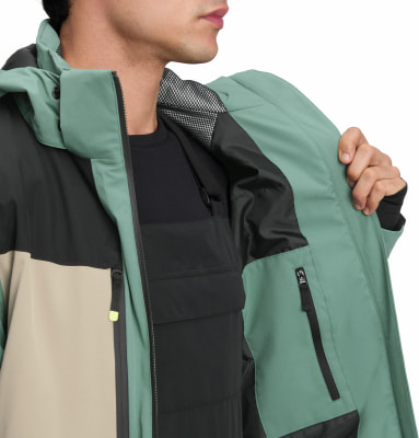 Mann in grüner Jacke mit schwarzen und beigen Einsätzen zeigt Innentasche.