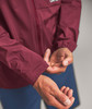 Ein Mann richtet den Ärmel einer weinroten Jacke, im Hintergrund blaue Hosen.