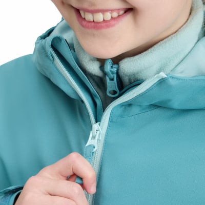 Ein Mädchen schließt ihre blaugrüne Jacke mit einem weißen Reißverschluss am Hals.