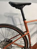 Detail des hinteren Teils eines orangefarbenen Fahrrads mit Sattel und Rädern.