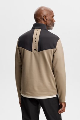 Ein Mann trägt von hinten eine beige Jacke mit schwarzen Einsätzen und Logo.