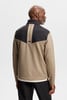 Ein Mann trägt von hinten eine beige Jacke mit schwarzen Einsätzen und Logo.