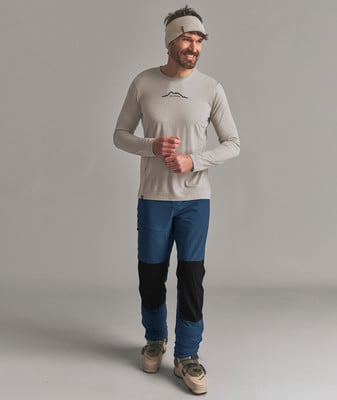 Ein Mann mit langärmeligem Shirt und blauen Hosen mit schwarzen Einsätzen, trägt Skischuhe. Ein Mann mit langärmeligem Shirt und blauen Hosen mit schwarzen Einsätzen, trägt Skischuhe.