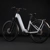 Ein silbernes E-Bike mit schwarzen Rädern und Schutzblechen vor dunklem Hintergrund.