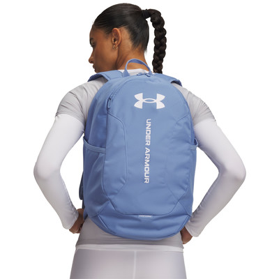 Egy copfos lány visel kék Under Armour hátizsákot a hátán. Egy copfos lány visel kék Under Armour hátizsákot a hátán.