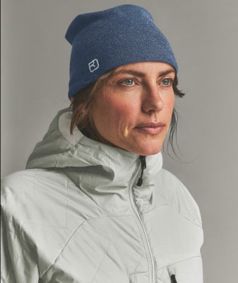 Eine Frau mit blauer Mütze und hellgrauer Kapuzenjacke blickt nach rechts.