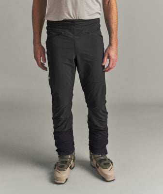 Mann in schwarzer Skihose und hellbeigen Skischuhen.
