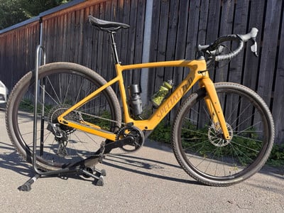 Ein gelbes Gravelbike mit schwarzen Details auf einem Ständer vor einem Holzzaun. Ein gelbes Gravelbike mit schwarzen Details auf einem Ständer vor einem Holzzaun.